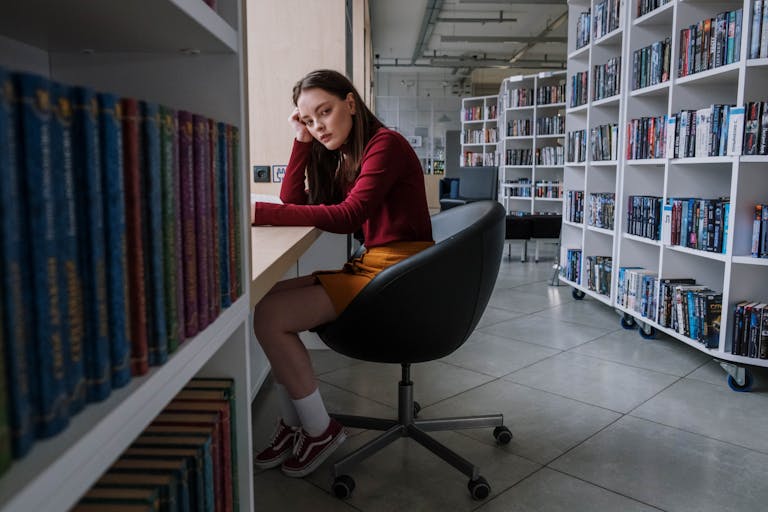 Teenage girl sitting and reading in a contemporary library. Bookshelves line the room.